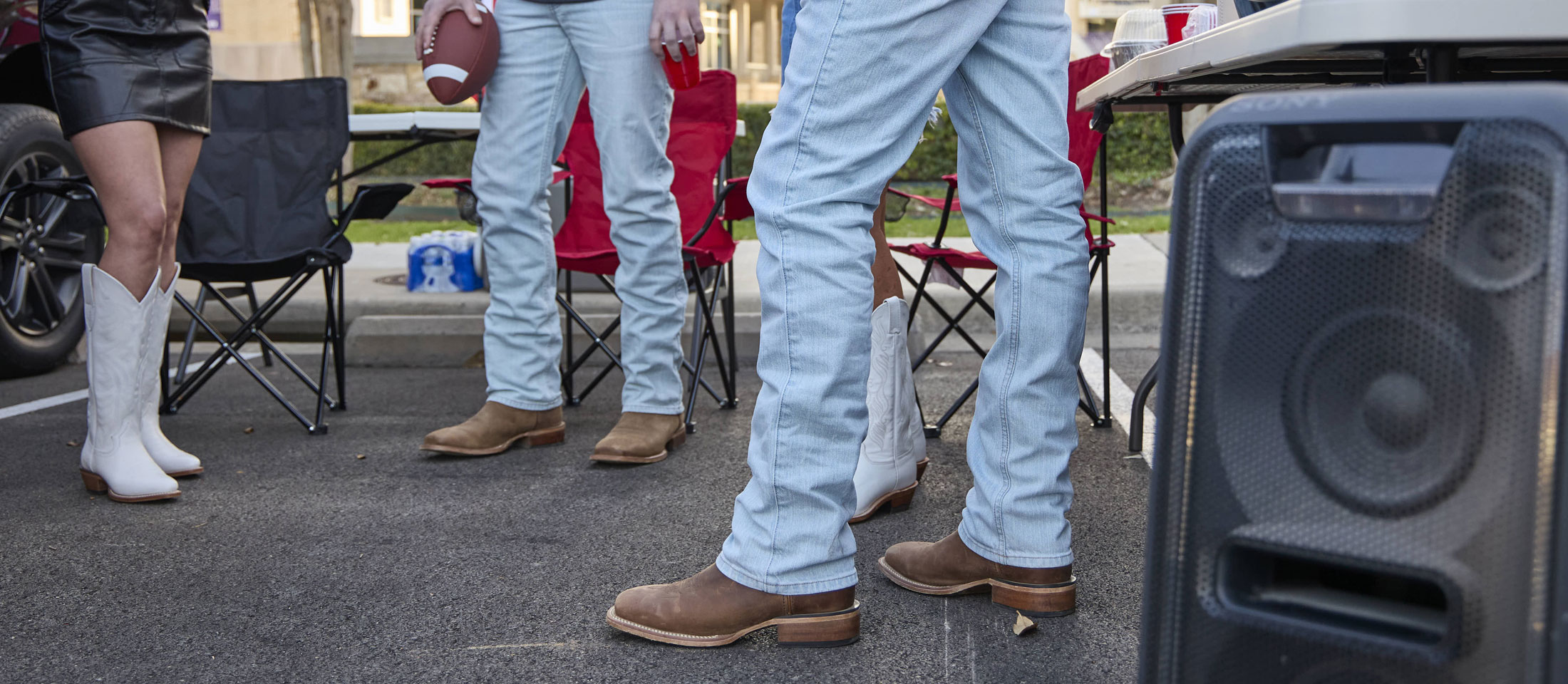 A group of young adults wearing Justin Boots while tailgating at a football game.